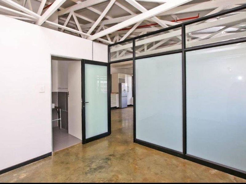 Modern office space featuring industrial-style exposed ceiling trusses, polished concrete floors, and sleek black-framed frosted glass partitions for a contemporary professional aesthetic.