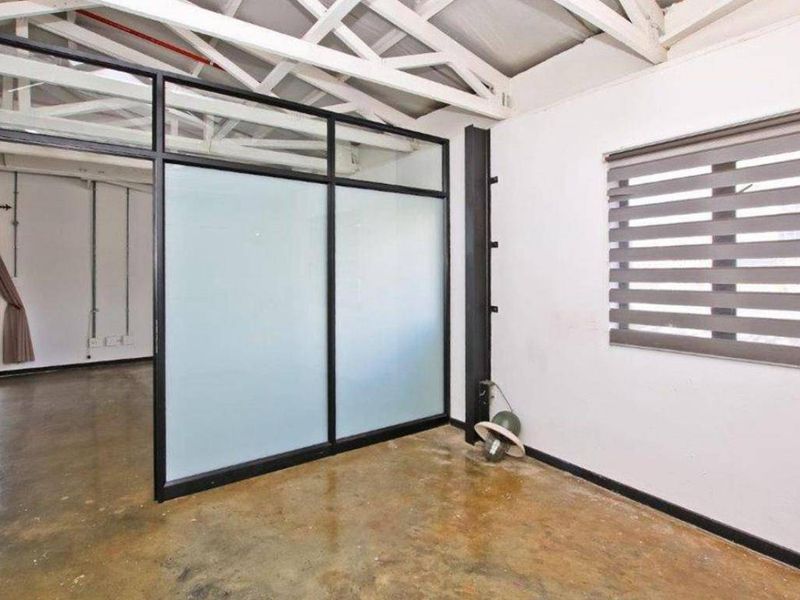An empty office space featuring polished concrete floors, exposed roof trusses, and a modern black-framed frosted glass partition for privacy.