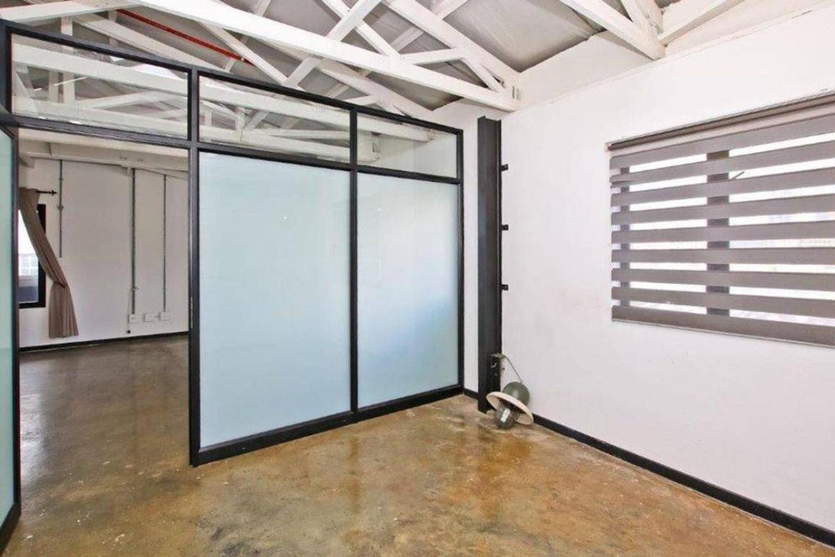 An empty office space featuring polished concrete floors, exposed roof trusses, and a modern black-framed frosted glass partition for privacy.