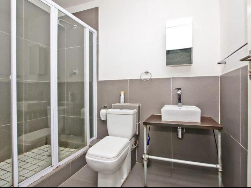 A clean, modern bathroom featuring a glass-enclosed shower, a white toilet, and a vessel sink mounted on a metal-frame vanity.