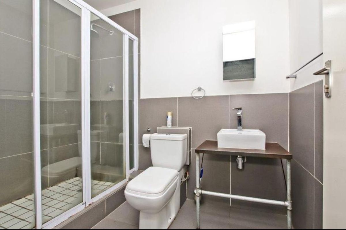 A clean, modern bathroom featuring a glass-enclosed shower, a white toilet, and a vessel sink mounted on a metal-frame vanity.