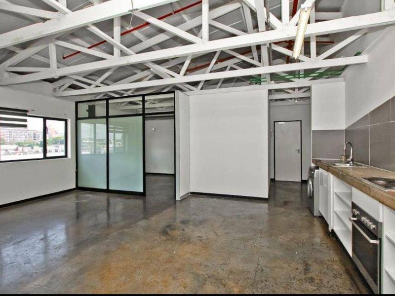 Spacious open-plan apartment featuring industrial-style exposed steel trusses, polished concrete floors, and a functional kitchen area with built-in appliances.