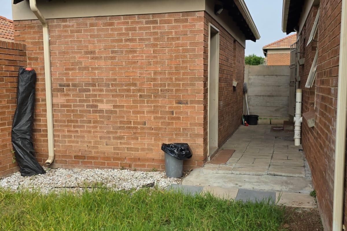 A side view of the property showing brick exterior walls, tiled roofing, and a paved walkway leading to the rear garden area.