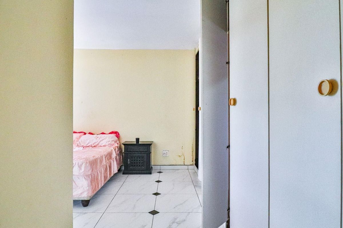 A bedroom featuring built-in cupboards and tiled flooring, showing signs of wear on the walls requiring maintenance.