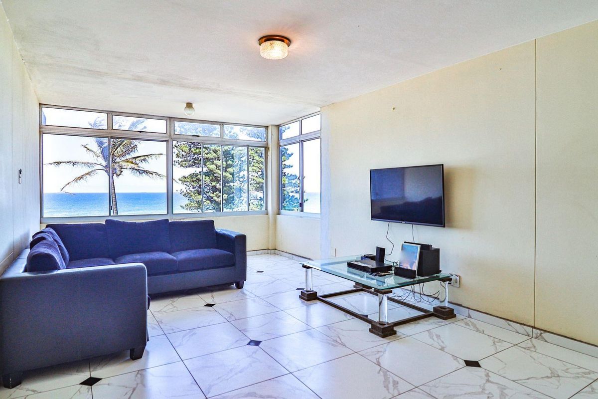 A living room featuring large windows with ocean views, tiled flooring, and a wall-mounted television.