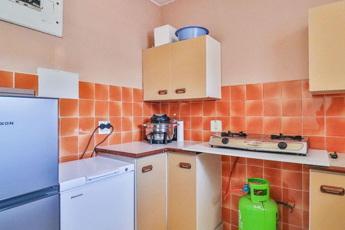 A compact kitchen featuring dated cabinetry, orange ceramic wall tiles, and a gas hob setup with laminate countertops.