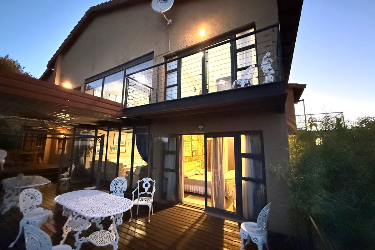 Rear view of the property featuring a wooden deck patio, ground floor access, and an upper-level balcony with metal railings.