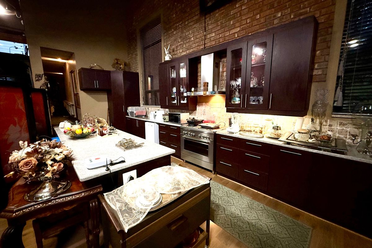 Spacious kitchen featuring dark wood cabinetry, granite countertops, a central island, and an exposed brick wall, creating a warm and industrial aesthetic.