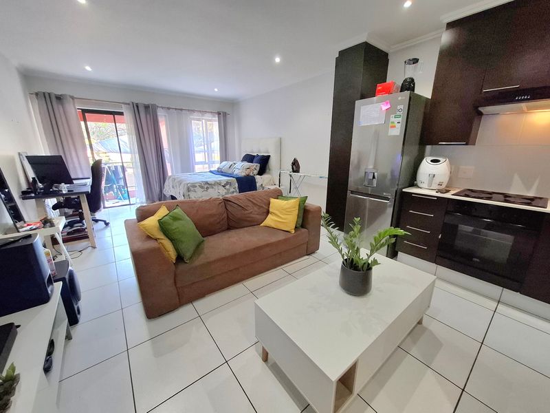 Open-plan studio apartment featuring a modern kitchen with dark cabinetry, tiled flooring, and direct access to a private balcony.