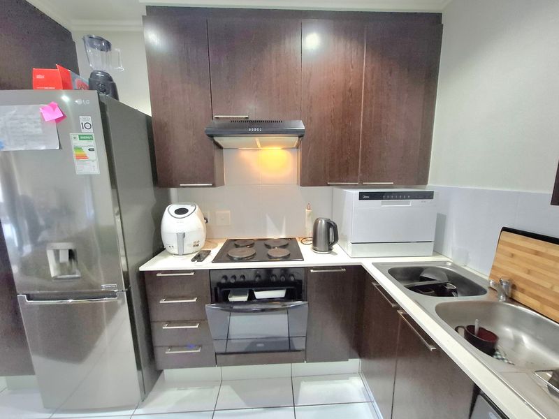 Compact kitchen featuring dark wood cabinetry, electric hob with extractor fan, built-in oven, and a double stainless steel sink with tiled splashback.