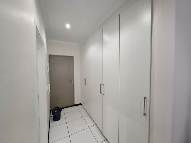 A clean, minimalist hallway featuring white tiled flooring and extensive built-in floor-to-ceiling storage cupboards.