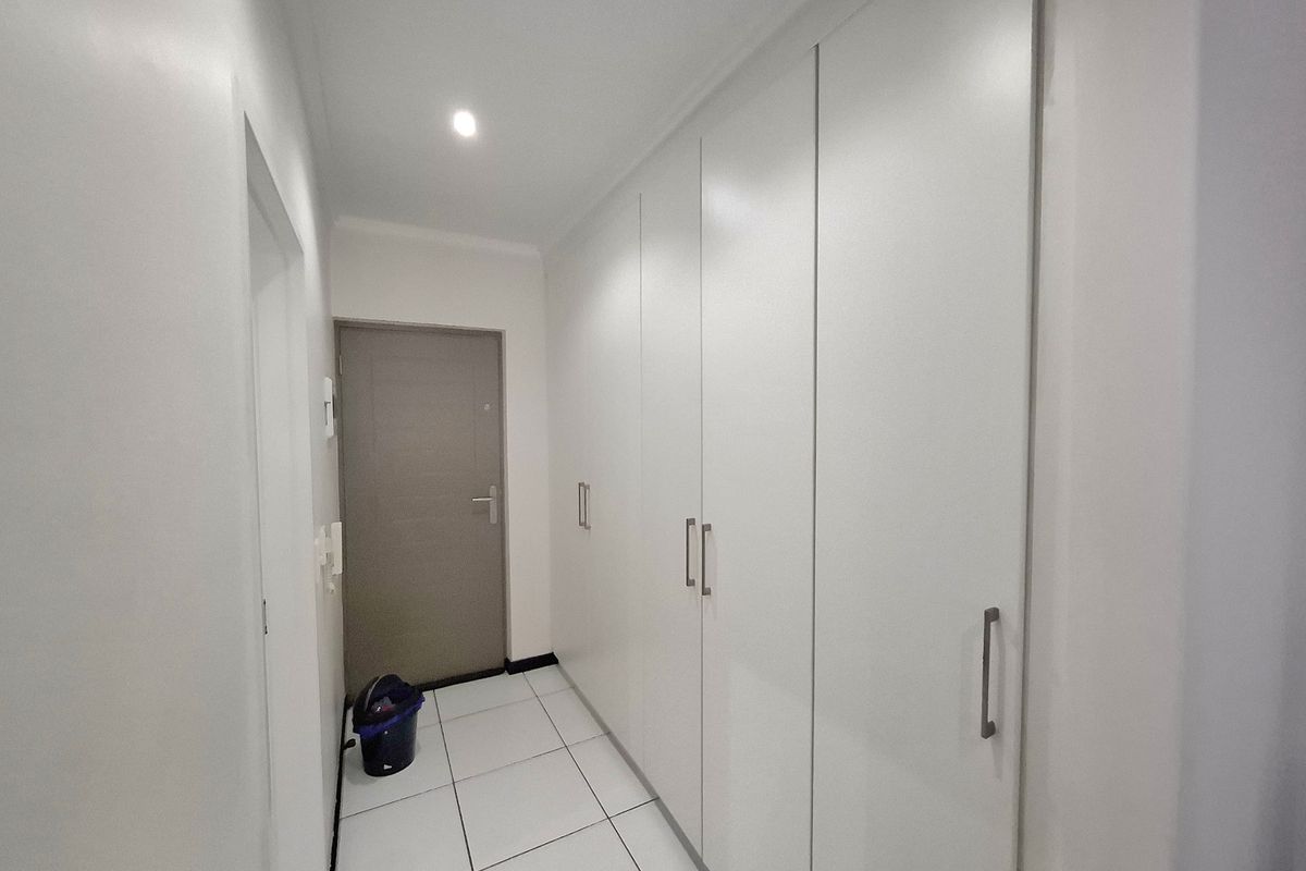 A clean, minimalist hallway featuring white tiled flooring and extensive built-in floor-to-ceiling storage cupboards.