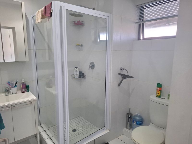 A functional bathroom featuring a white vanity cabinet, a glass-enclosed shower, and a standard toilet with tiled finishes throughout.