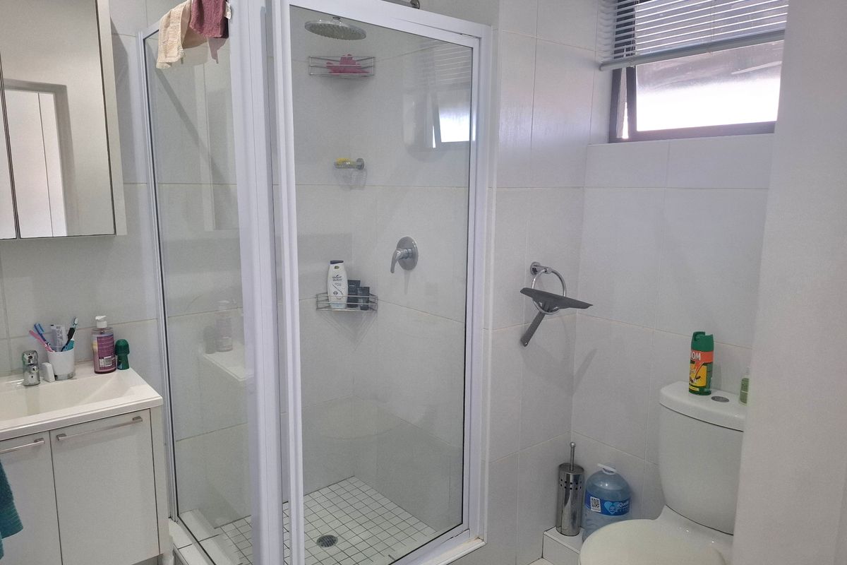 A functional bathroom featuring a white vanity cabinet, a glass-enclosed shower, and a standard toilet with tiled finishes throughout.