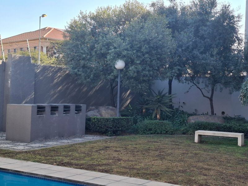 Outdoor pool area featuring a built-in braai, stone bench seating, and established garden landscaping within a walled perimeter.