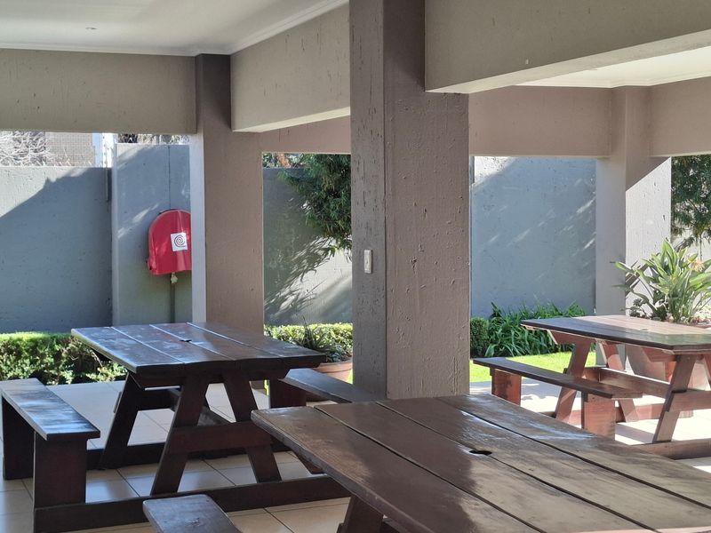A covered outdoor patio area featuring tiled flooring, concrete support columns, and a wall-mounted fire hose reel, suitable for communal or private outdoor seating.