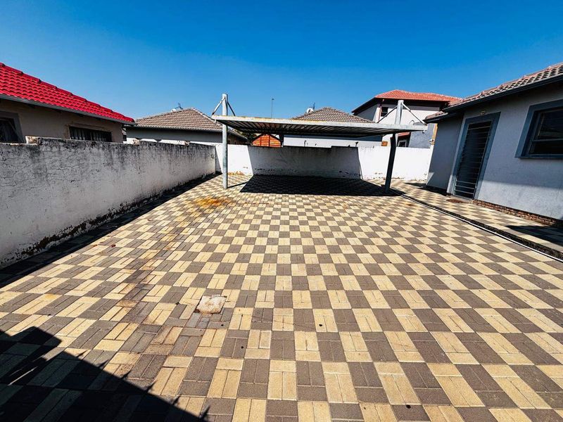 A paved rear courtyard area featuring a metal carport structure and enclosed by boundary walls.