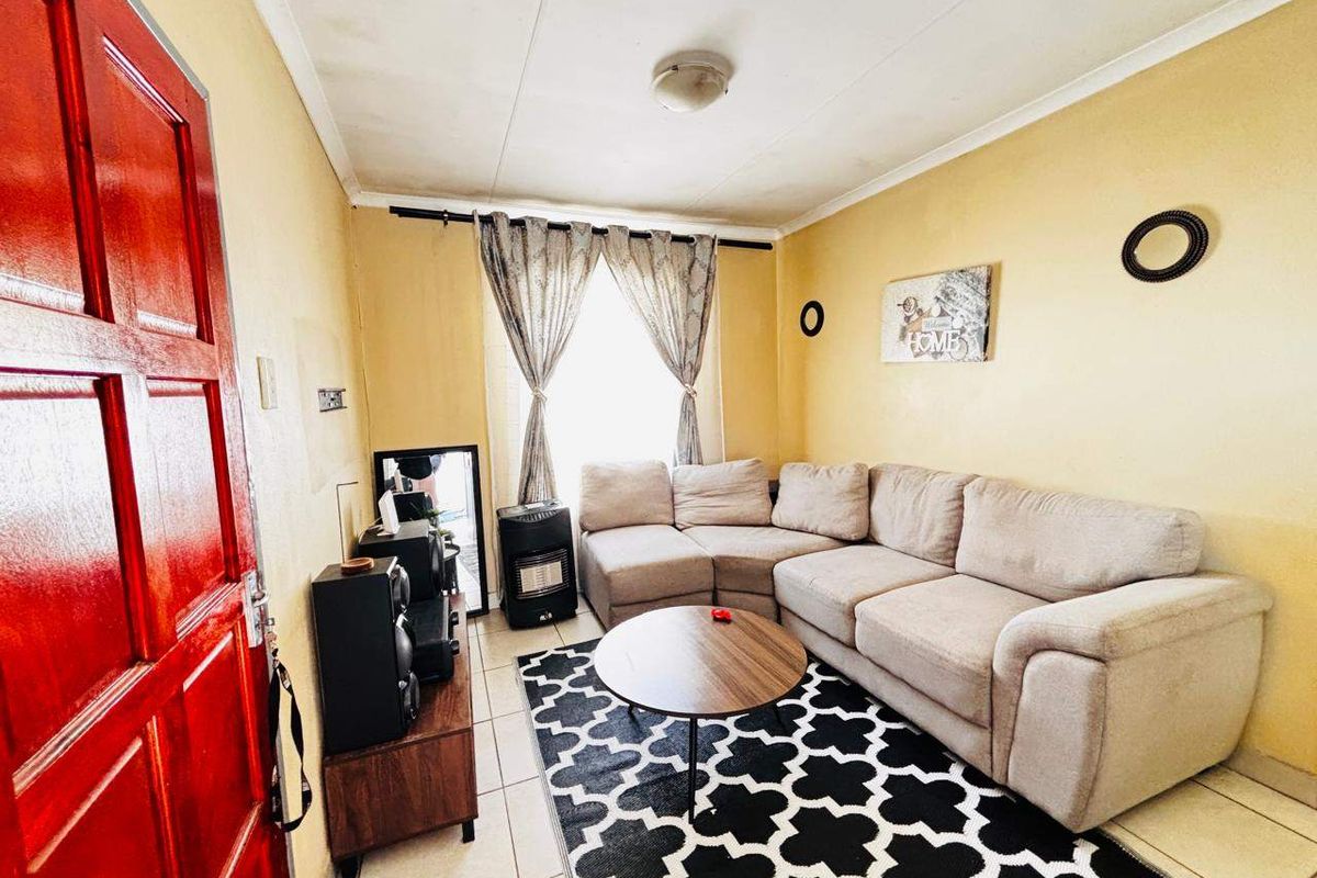 A compact living room featuring tiled flooring and a bright red entrance door, offering a functional space with potential for cosmetic updates.
