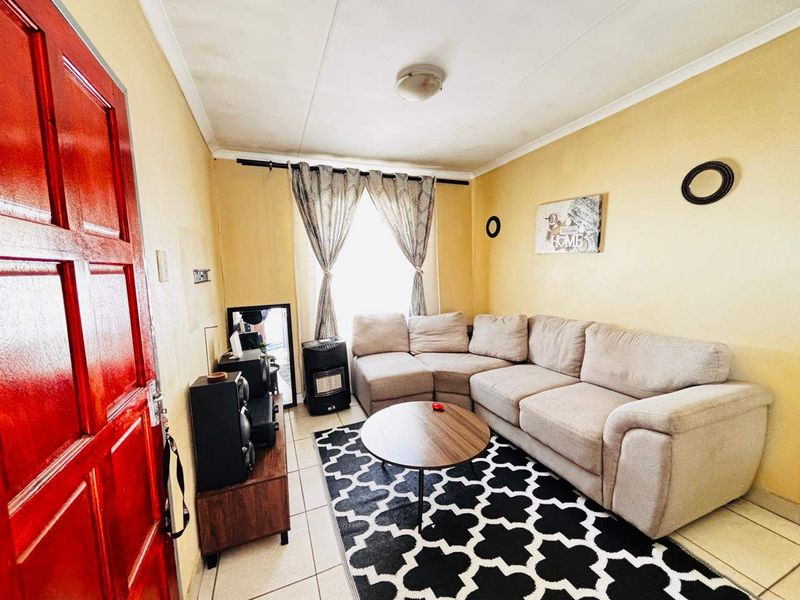 A compact living room featuring tiled flooring and a bright red entrance door, offering a functional space with potential for cosmetic updates.