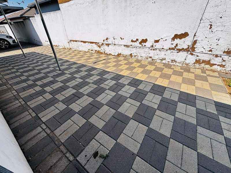 A paved outdoor area featuring a dual-tone block driveway and a boundary wall requiring maintenance and repainting.