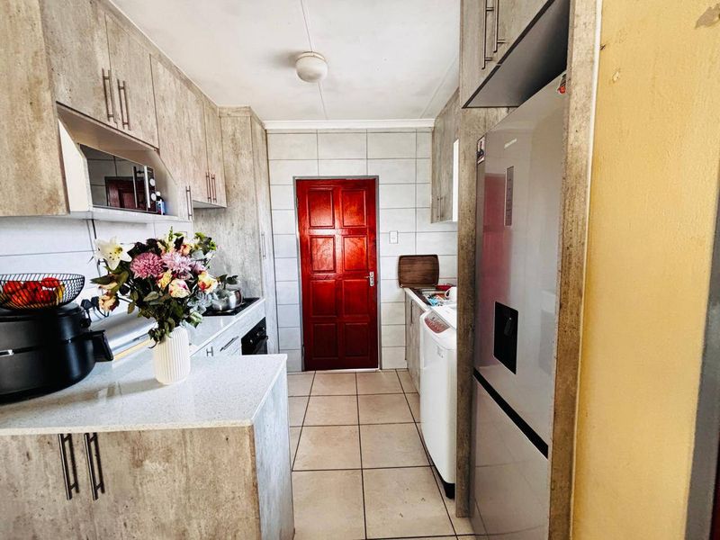 A functional kitchen featuring laminate cabinetry, stone-look countertops, tiled backsplash, and built-in cooking appliances with tiled flooring throughout.