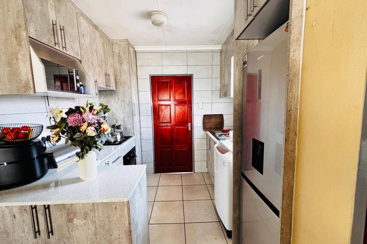 A functional kitchen featuring laminate cabinetry, stone-look countertops, tiled backsplash, and built-in cooking appliances with tiled flooring throughout.