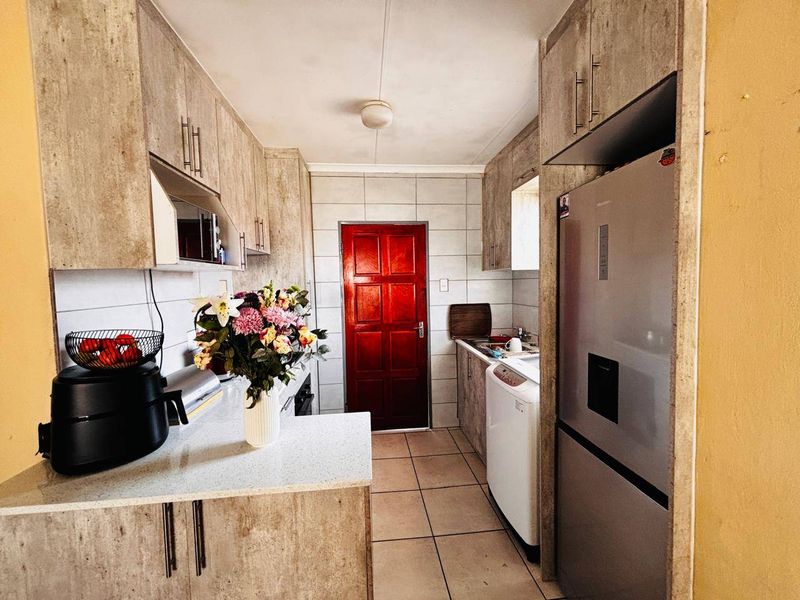 A functional galley-style kitchen featuring laminate cabinetry, stone-look countertops, tiled backsplash, and tiled flooring with direct access to an exterior door.