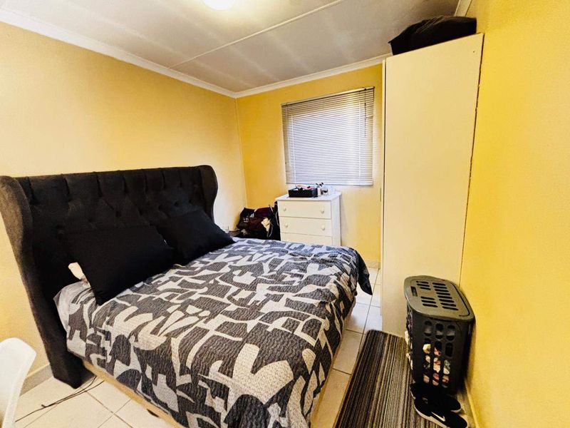 A functional bedroom featuring tiled flooring, a coved ceiling, and a window fitted with venetian blinds.