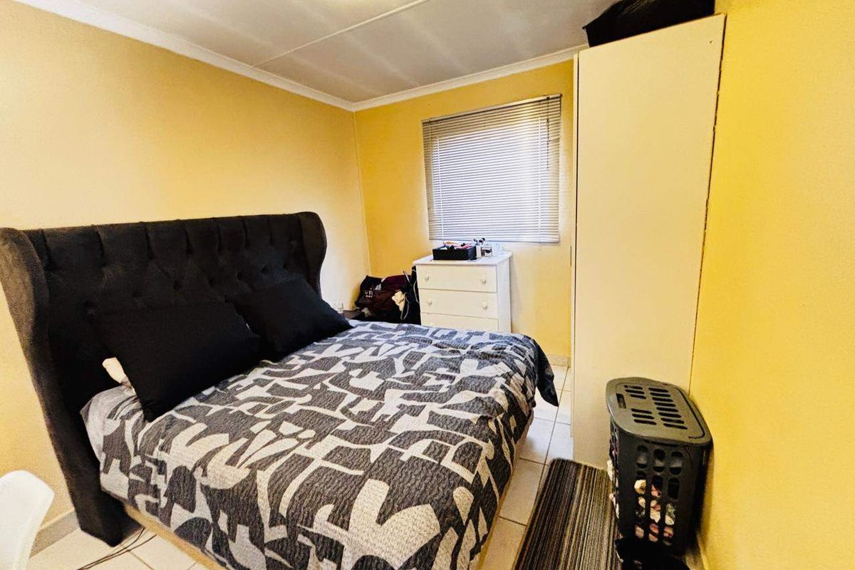 A functional bedroom featuring tiled flooring, a coved ceiling, and a window fitted with venetian blinds.