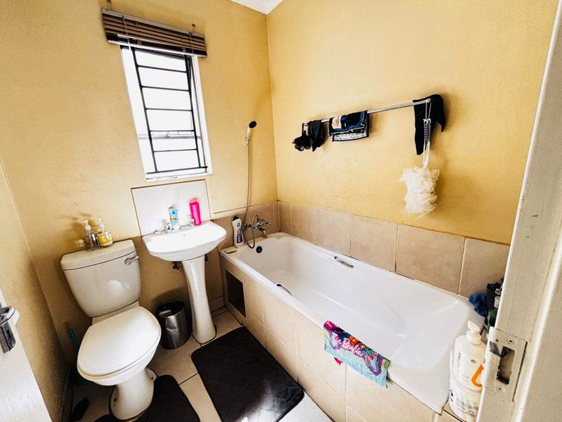 A functional bathroom featuring a pedestal basin, toilet, and bathtub with a tiled splashback, offering potential for modernization and cosmetic updates.