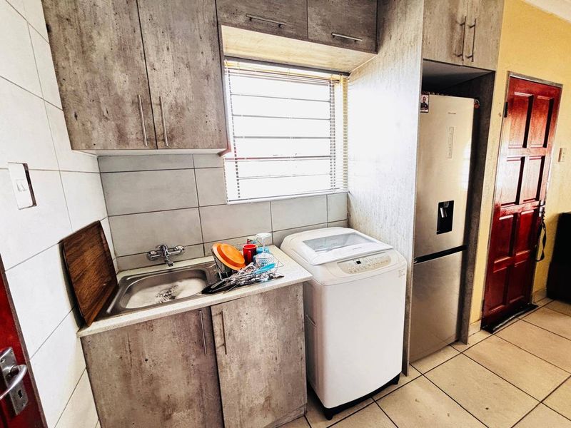 A functional laundry area featuring built-in cabinetry, a stainless steel sink, tiled backsplash, and tiled flooring.