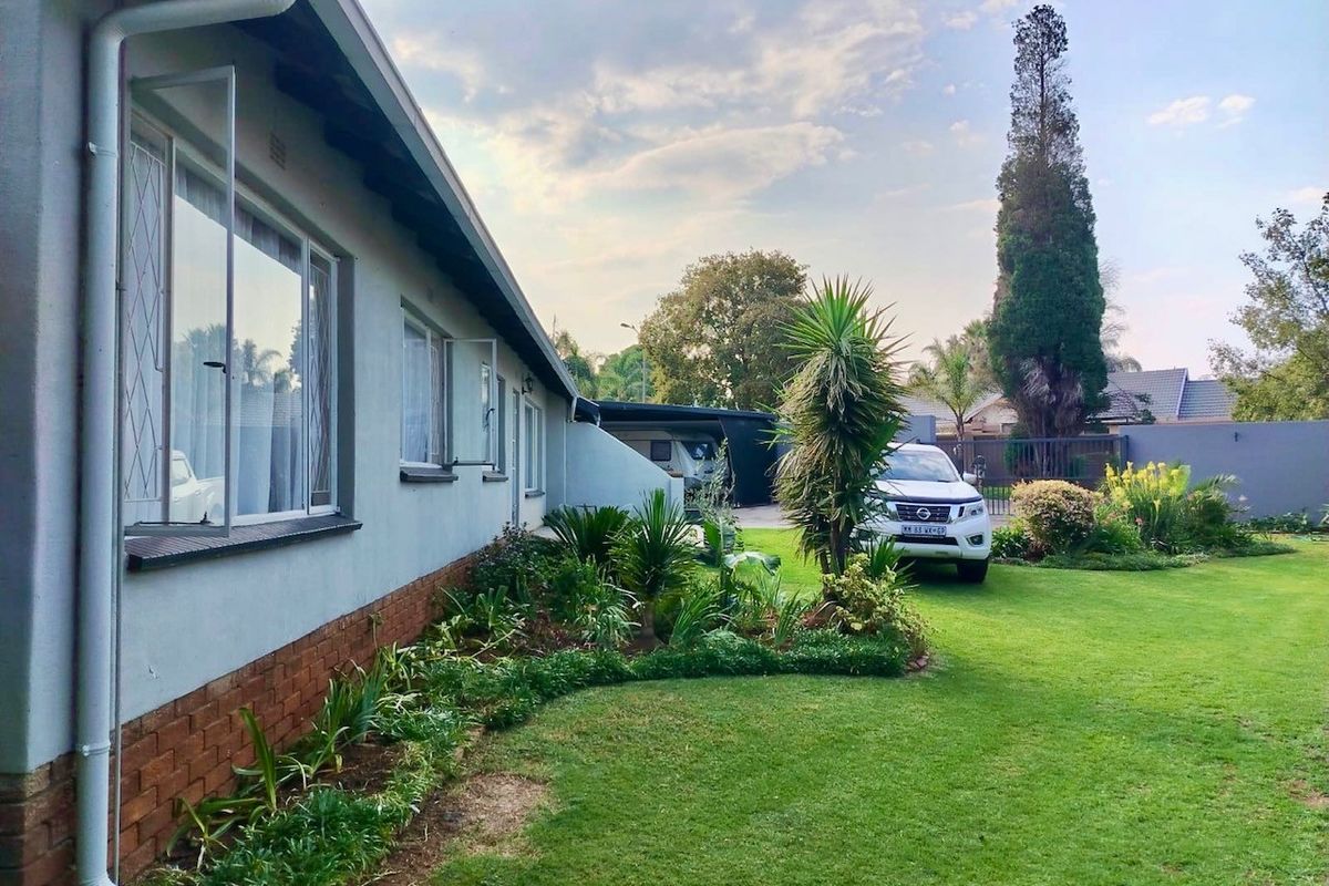 A well-maintained rear garden featuring a lush lawn, landscaped garden beds, and a clear view of the property's side elevation and carport.