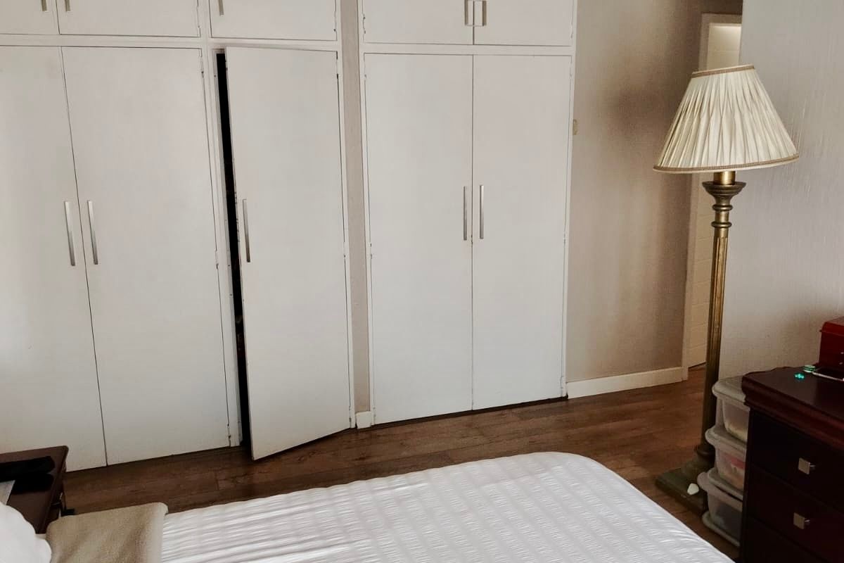 A bedroom featuring built-in white cupboards with overhead storage and laminate flooring.