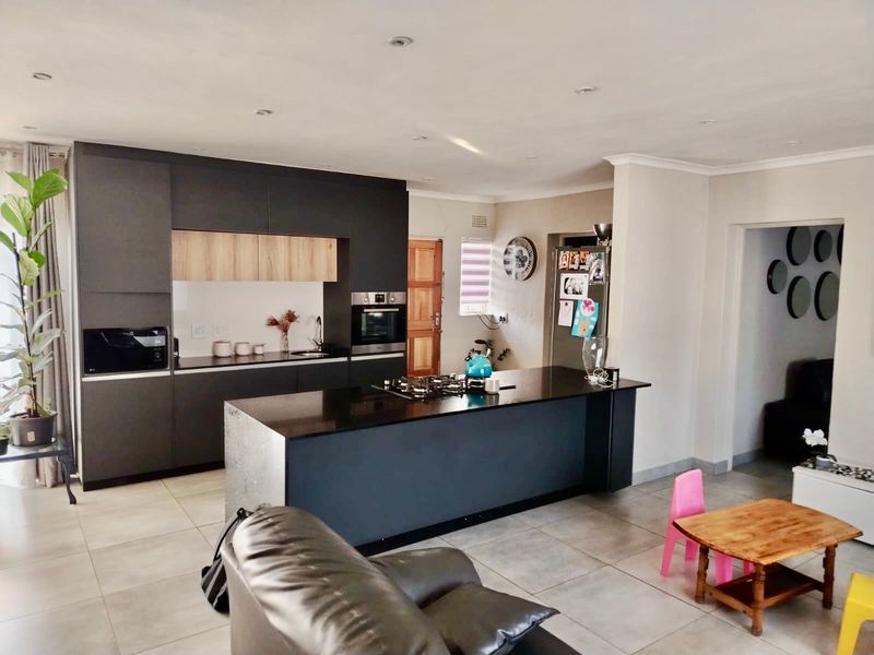 Modern open-plan kitchen featuring dark cabinetry, a central island with a gas hob, and sleek tiled flooring, seamlessly integrated with the living area.