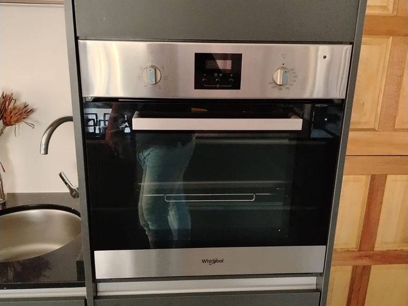 A modern kitchen section featuring a built-in Whirlpool oven and a stainless steel sink with dark cabinetry.