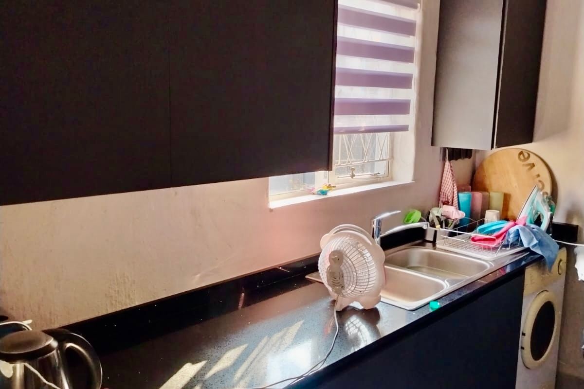 A compact kitchen featuring dark cabinetry, black granite countertops, a stainless steel double sink, and tiled flooring with a window roller blind.