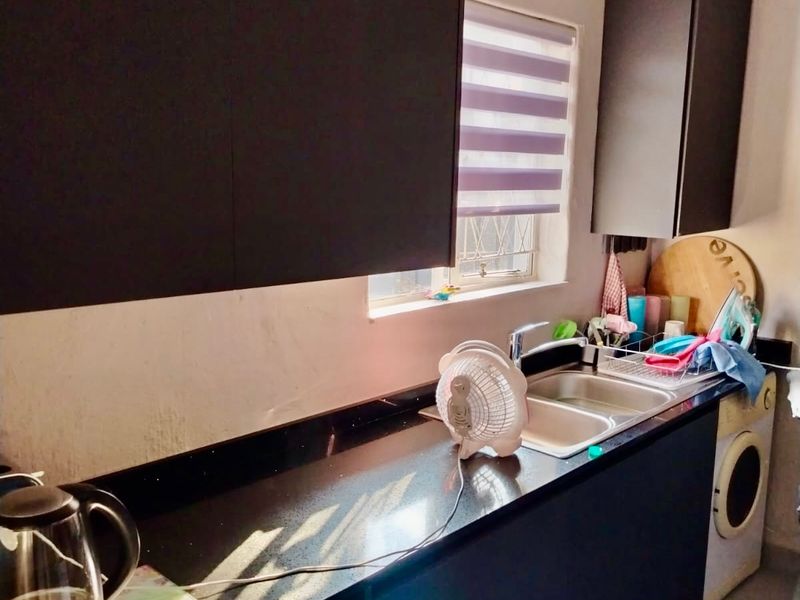 A compact kitchen featuring dark cabinetry, black granite countertops, a stainless steel double sink, and tiled flooring with a window roller blind.