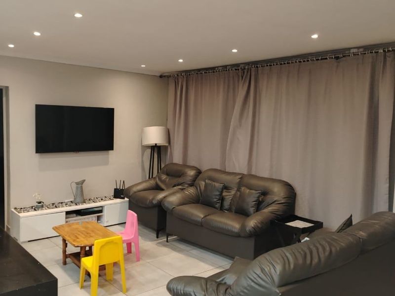 A well-lit living room featuring neutral tiled flooring, recessed downlighting, and full-length curtain tracks, providing a functional and comfortable space.