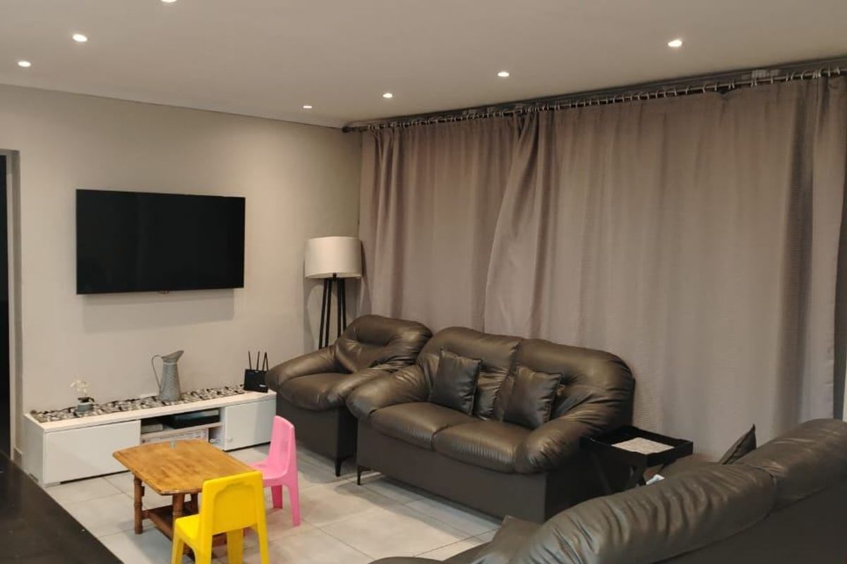 A well-lit living room featuring neutral tiled flooring, recessed downlighting, and full-length curtain tracks, providing a functional and comfortable space.