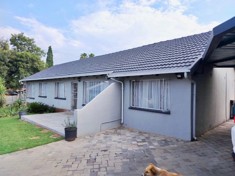 Front elevation of a single-story house featuring a tiled roof, paved driveway, and a concrete patio area with security features.