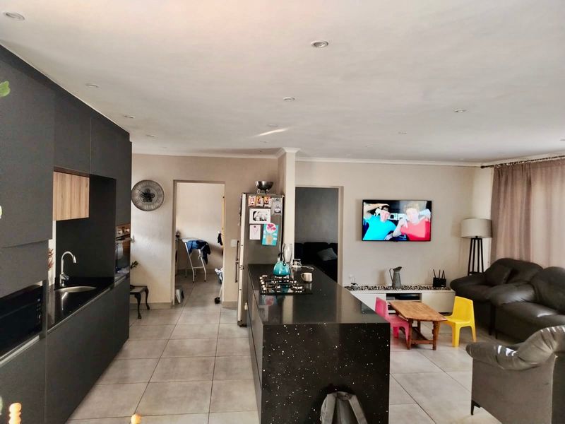 Spacious open-plan living area featuring a modern kitchen with a central island, gas hob, and sleek dark cabinetry, seamlessly flowing into the lounge space.