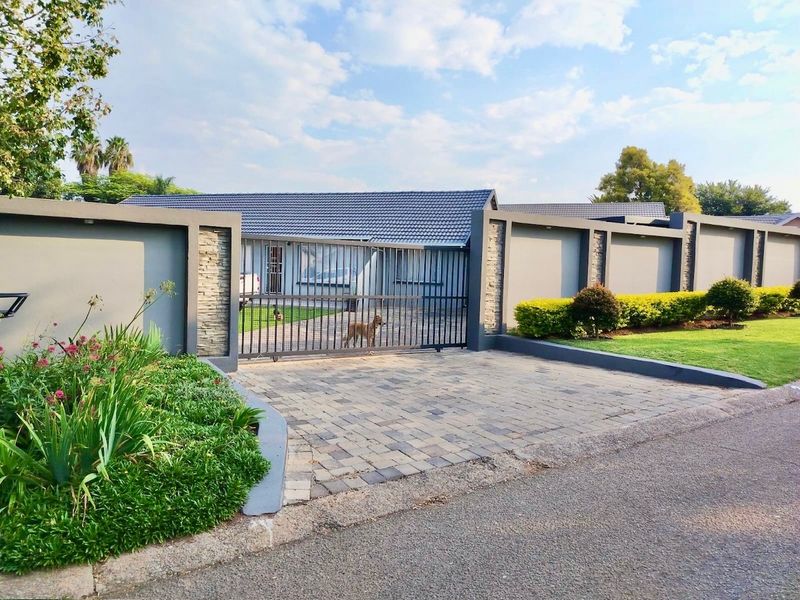 Front view of the property featuring a secure sliding gate, paved driveway, and modern perimeter wall with stone cladding accents.
