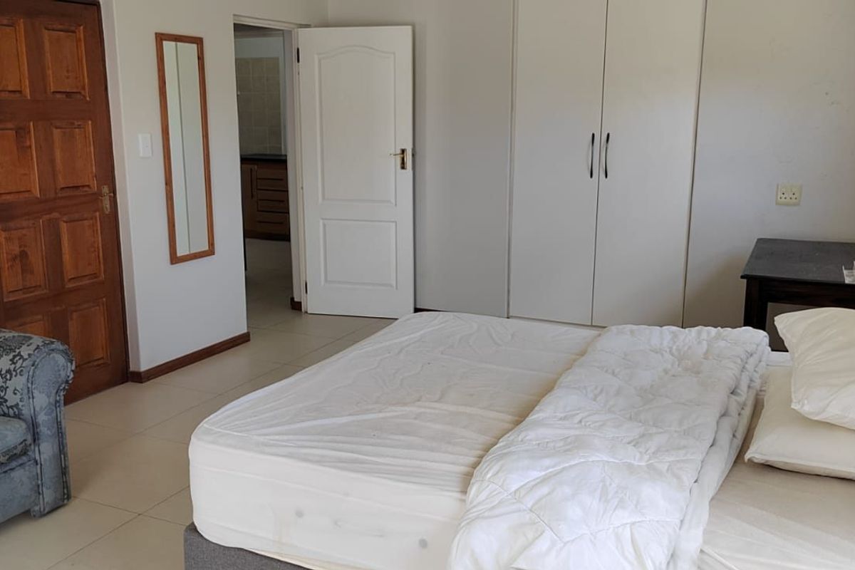 A spacious bedroom featuring built-in cupboards, tiled flooring, and direct access to an adjoining room.
