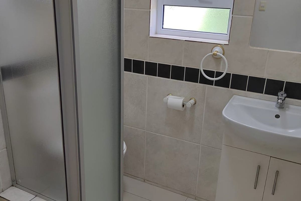 A functional bathroom featuring a shower enclosure, vanity basin, and neutral wall tiling with a decorative black accent border.