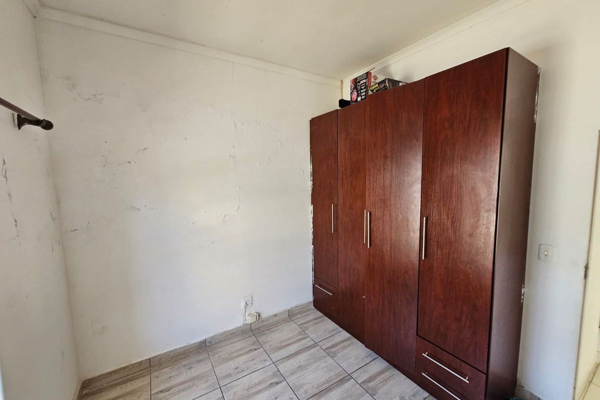 A bedroom featuring tiled flooring and a large built-in wooden wardrobe, showing signs of wear on the wall surfaces.