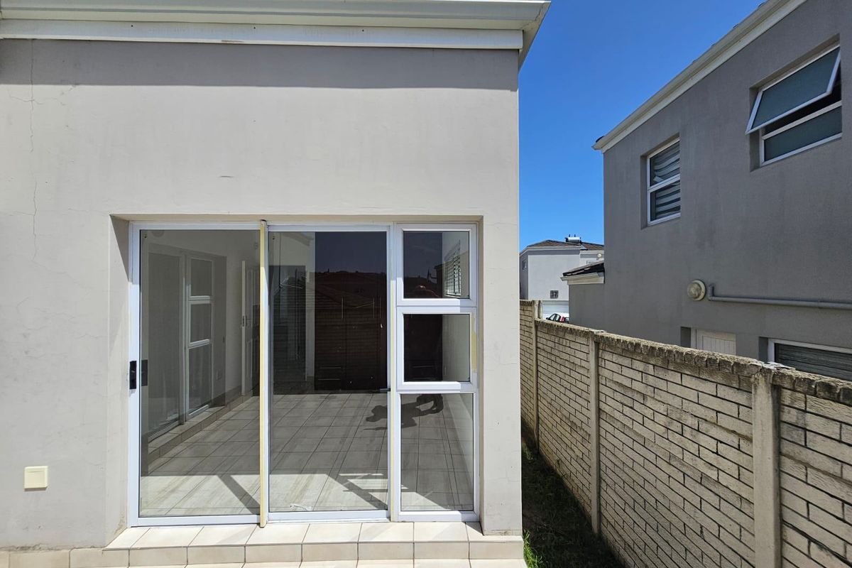 Rear view of the townhouse featuring a tiled patio area, sliding glass doors, and a brick boundary wall.