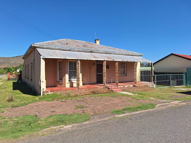Front elevation of a single-story house featuring a corrugated iron roof, covered veranda with brick pillars, and a metal security gate.