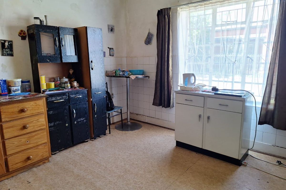 A dated kitchen area featuring tiled splashbacks, security bars on the window, and vinyl flooring, requiring cosmetic updates and wall repairs.