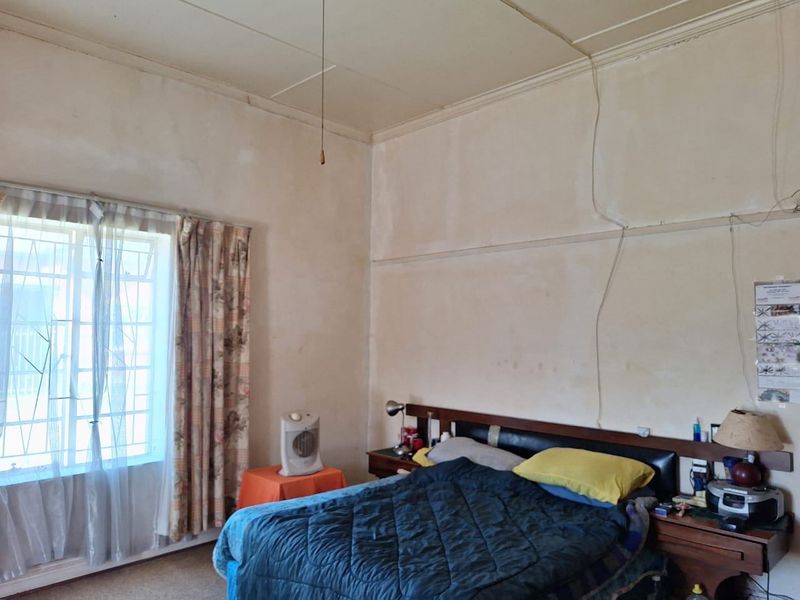 A bedroom featuring original picture rails and security bars on the window, currently requiring significant cosmetic renovation and wall repairs.