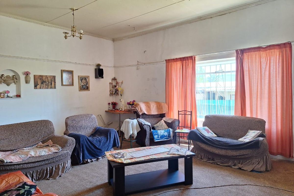 A living room featuring dated wall finishes, worn carpeting, and security bars on the window, offering potential for renovation and modernization.